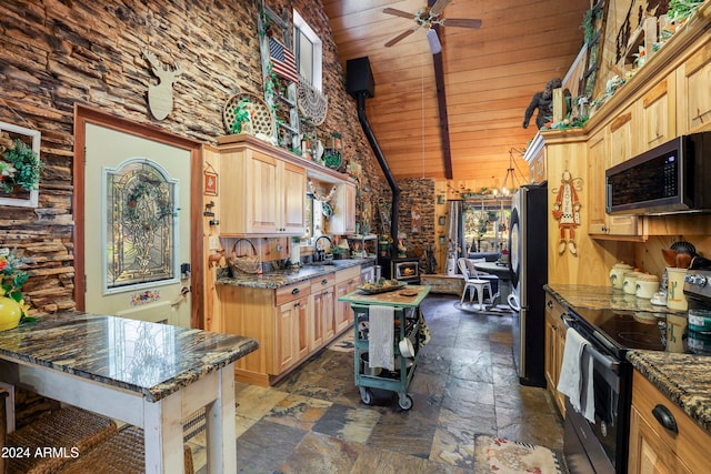 kitchen with light brown cabinets, stainless steel appliances, a wood stove, and dark stone countertops