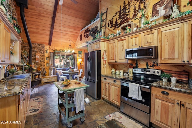 kitchen featuring vaulted ceiling with beams, dark stone countertops, sink, a wood stove, and stainless steel appliances