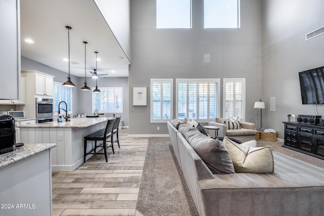 living room featuring sink, light hardwood / wood-style flooring, a towering ceiling, and ceiling fan