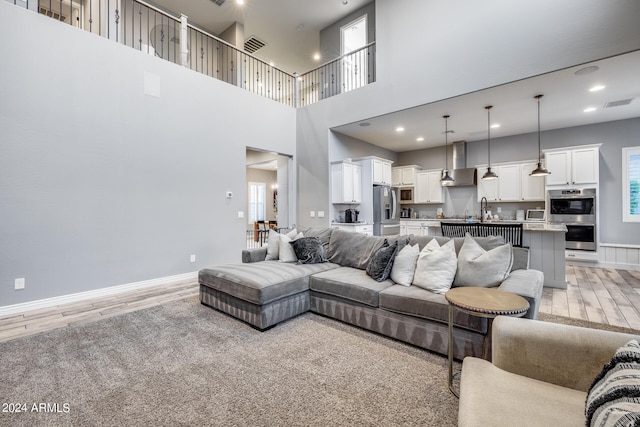 living room featuring a wealth of natural light, sink, light hardwood / wood-style floors, and a towering ceiling