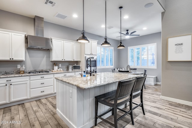 kitchen with light stone countertops, white cabinets, a kitchen island with sink, and hanging light fixtures