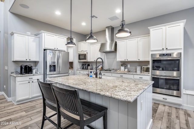 kitchen featuring stainless steel appliances, wall chimney range hood, and white cabinets