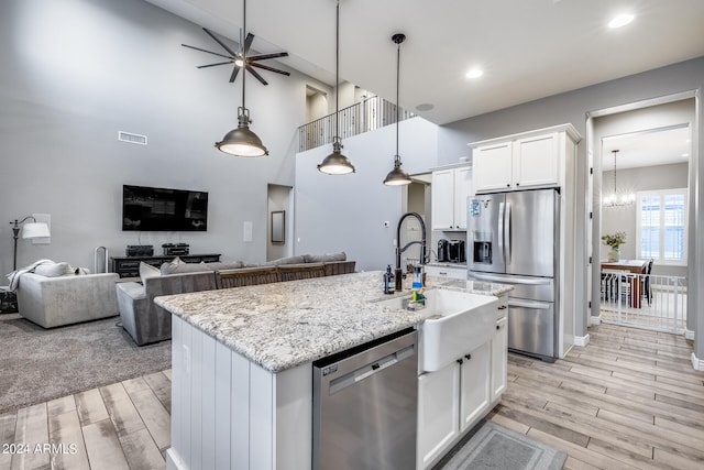 kitchen featuring an island with sink, hanging light fixtures, stainless steel appliances, light wood-type flooring, and white cabinetry