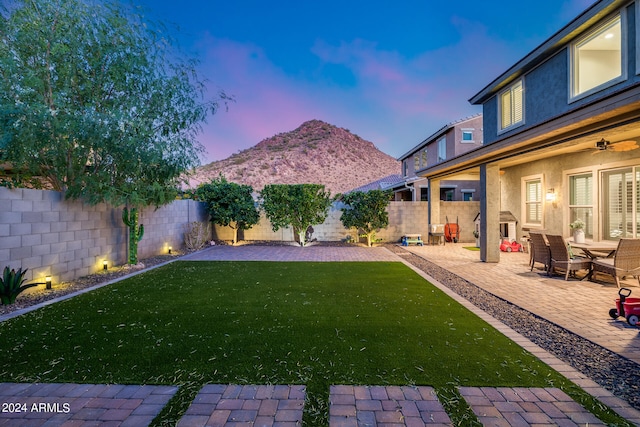 yard at dusk featuring a patio, a mountain view, and ceiling fan