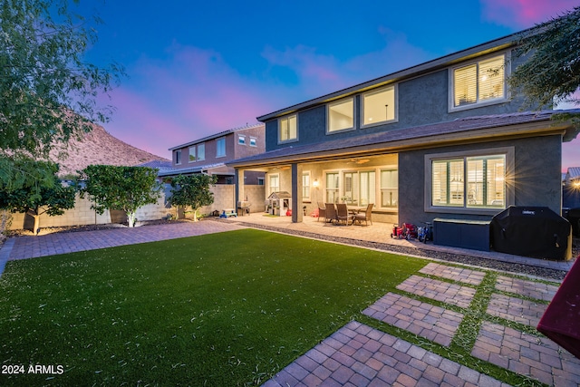 back house at dusk featuring a patio area and a yard