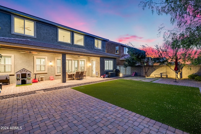 back house at dusk with a yard, ceiling fan, and a patio area