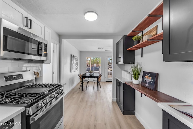 kitchen with open shelves, light wood-type flooring, light countertops, baseboards, and stainless steel appliances