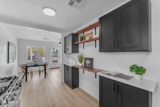kitchen featuring visible vents, open shelves, stainless steel gas stove, and dark cabinets