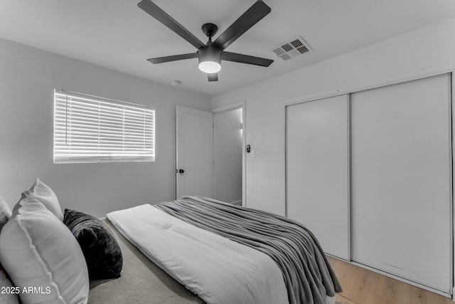 bedroom with a ceiling fan, visible vents, light wood finished floors, and a closet