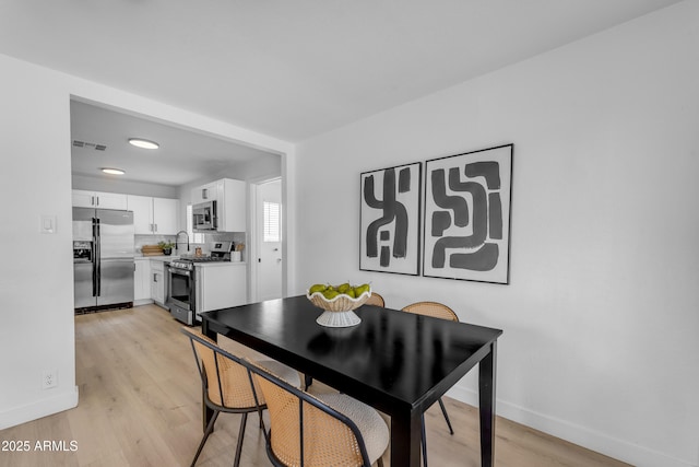 dining space with baseboards, light wood finished floors, and visible vents