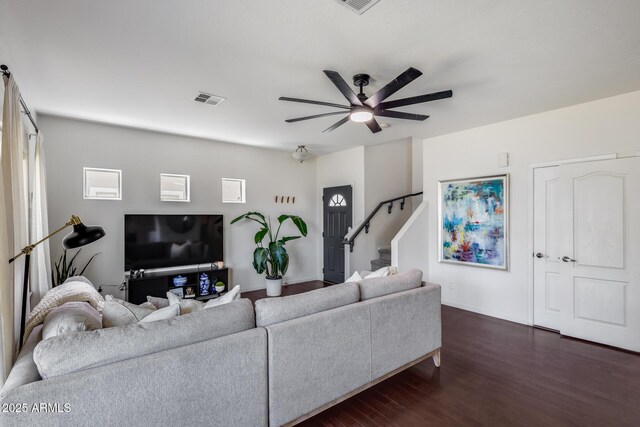 living area with a ceiling fan, visible vents, stairway, baseboards, and dark wood-type flooring
