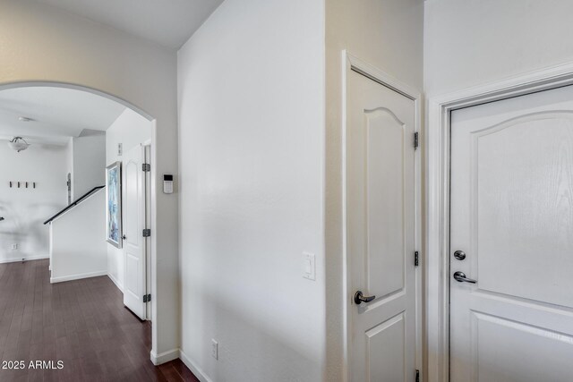 hall featuring dark wood-type flooring, arched walkways, and baseboards