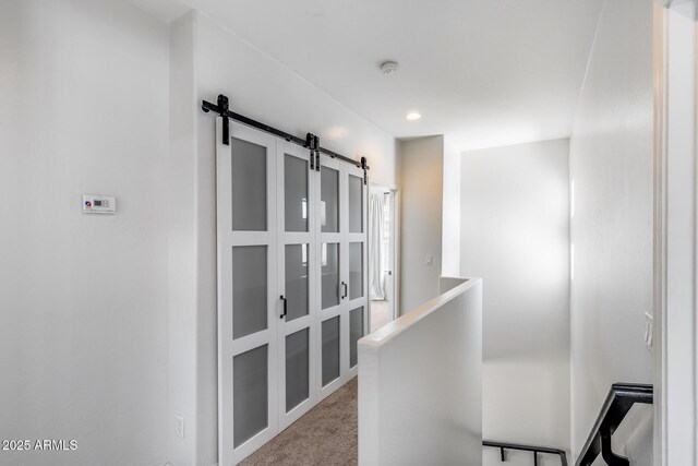 hallway with an upstairs landing, a barn door, and light colored carpet