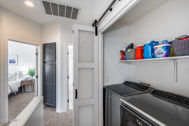 laundry area with laundry area, visible vents, a barn door, light carpet, and washer and dryer