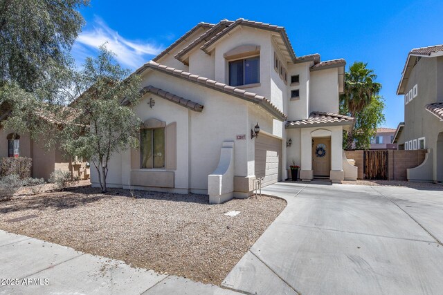 mediterranean / spanish house with fence, an attached garage, stucco siding, a tiled roof, and driveway