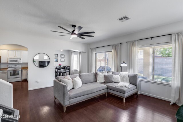 living room featuring visible vents, arched walkways, baseboards, and a ceiling fan