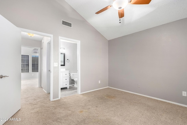 unfurnished bedroom with ceiling fan, vaulted ceiling, light carpet, and ensuite bath