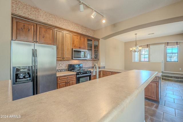 kitchen featuring pendant lighting, an inviting chandelier, decorative backsplash, stainless steel appliances, and brick wall