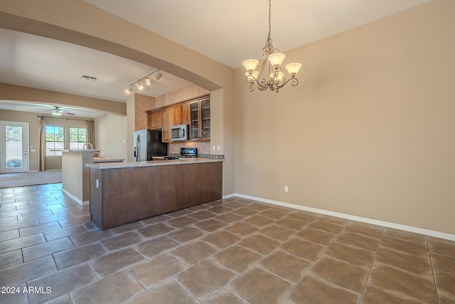 kitchen with kitchen peninsula, appliances with stainless steel finishes, rail lighting, decorative backsplash, and ceiling fan with notable chandelier