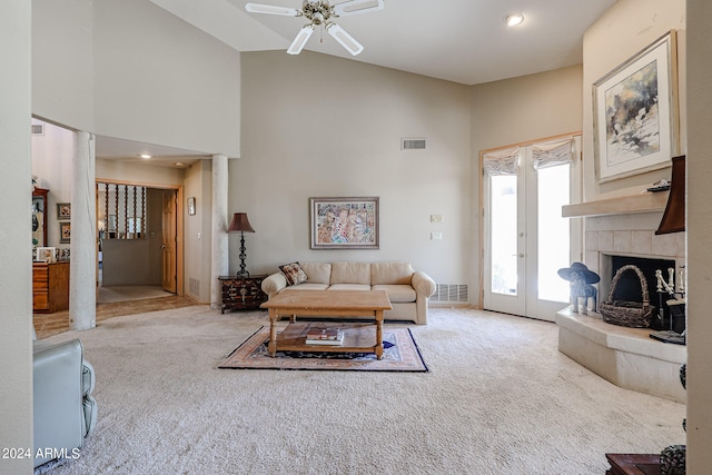 carpeted living room with ceiling fan, a tile fireplace, high vaulted ceiling, and french doors