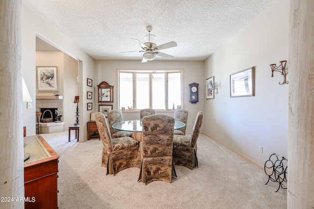 dining area featuring a tile fireplace, ceiling fan, light colored carpet, and a textured ceiling