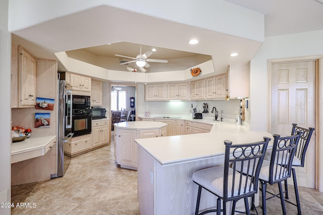 kitchen featuring ceiling fan, a raised ceiling, kitchen peninsula, a breakfast bar area, and black appliances