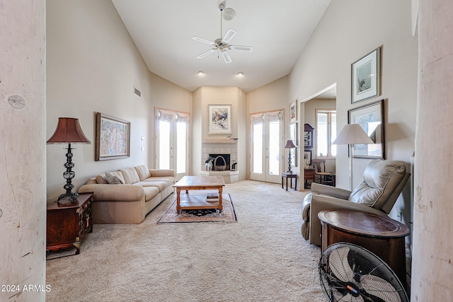 carpeted living room with ceiling fan, french doors, a towering ceiling, and a tiled fireplace