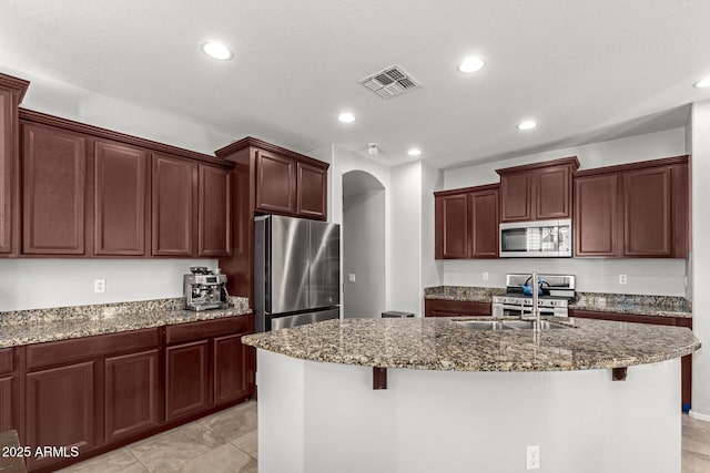 kitchen with appliances with stainless steel finishes, a breakfast bar, an island with sink, and dark stone countertops