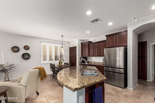 kitchen with sink, dark brown cabinets, hanging light fixtures, stainless steel fridge, and dark stone counters