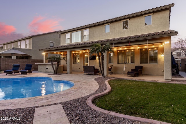 back house at dusk featuring a fenced in pool, a patio, and an outdoor kitchen