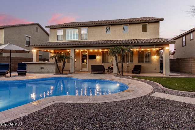 pool at dusk featuring a patio and an outdoor bar