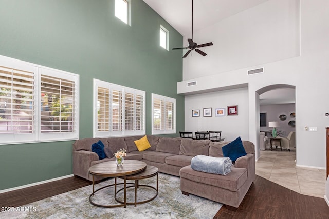 living room with ceiling fan, wood-type flooring, and a towering ceiling