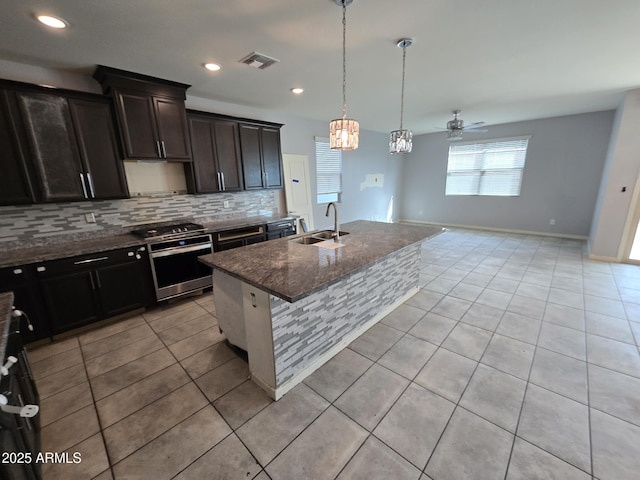 kitchen with a center island with sink, visible vents, stove, a sink, and dark stone counters