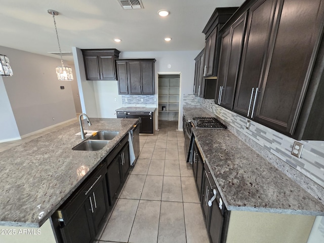 kitchen with light tile patterned floors, stone counters, a kitchen island with sink, a sink, and decorative light fixtures