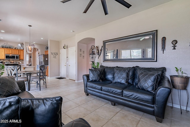 living area with a ceiling fan, baseboards, arched walkways, and light tile patterned flooring