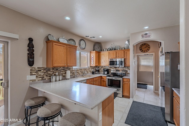 kitchen featuring stainless steel appliances, light countertops, a sink, decorative backsplash, and a peninsula