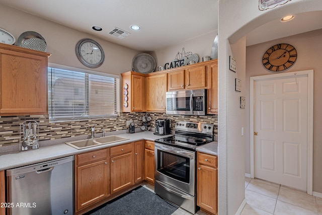 kitchen with a sink, decorative backsplash, light tile patterned floors, stainless steel appliances, and light countertops