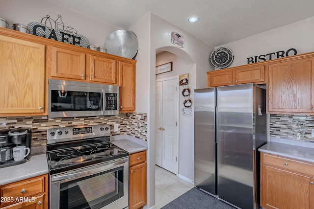 kitchen with light tile patterned flooring, arched walkways, light countertops, backsplash, and appliances with stainless steel finishes