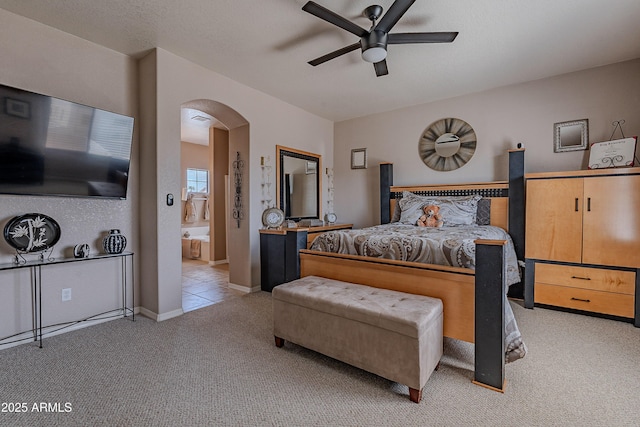 bedroom with arched walkways, ensuite bathroom, baseboards, light colored carpet, and ceiling fan