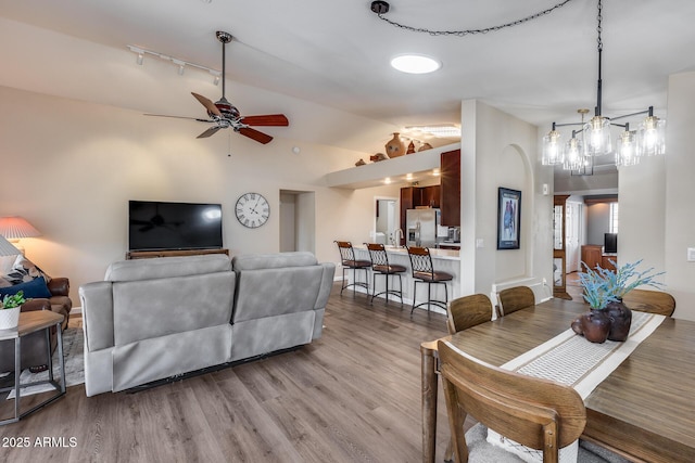 living room featuring ceiling fan with notable chandelier, vaulted ceiling, wood finished floors, and rail lighting