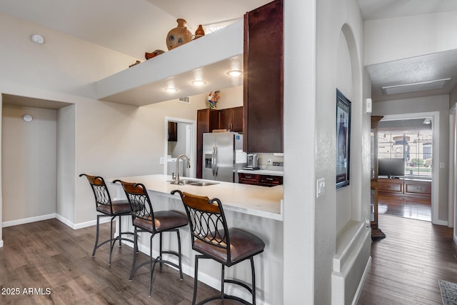 kitchen with a breakfast bar, dark wood finished floors, a sink, and stainless steel fridge with ice dispenser