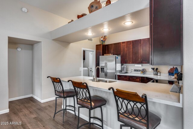 kitchen with dark wood-style floors, stainless steel refrigerator with ice dispenser, light countertops, and a breakfast bar area