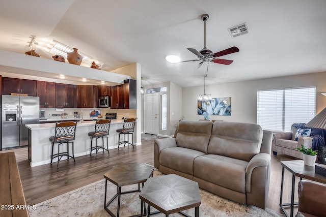 living room with a healthy amount of sunlight, wood finished floors, visible vents, and ceiling fan with notable chandelier