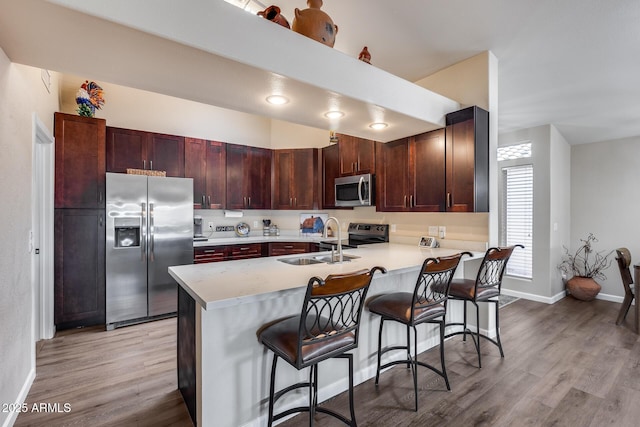 kitchen with stainless steel appliances, light countertops, a sink, a peninsula, and light wood-style flooring