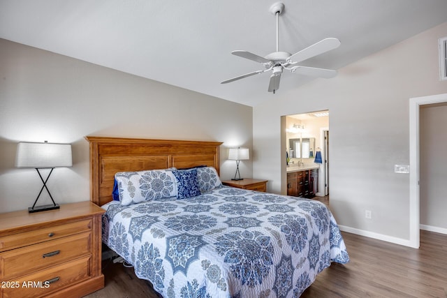 bedroom featuring dark wood finished floors, lofted ceiling, ensuite bath, baseboards, and ceiling fan