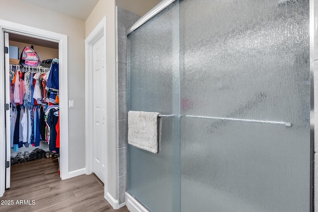 full bath featuring a walk in closet, baseboards, wood finished floors, and a stall shower
