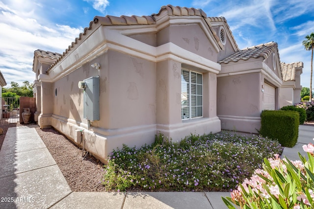view of side of home with stucco siding, a tiled roof, and a garage
