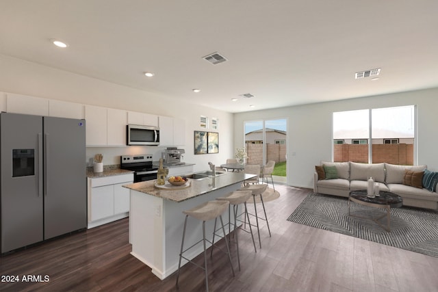 kitchen featuring dark wood-type flooring, white cabinets, a kitchen breakfast bar, a center island with sink, and appliances with stainless steel finishes