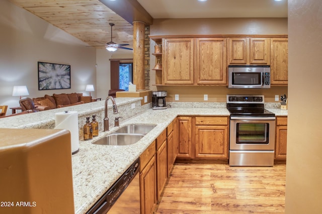 kitchen featuring light wood-style flooring, light stone counters, stainless steel appliances, and a sink