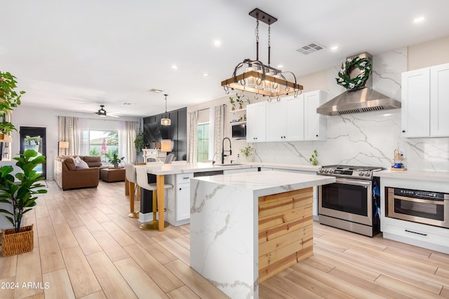 kitchen featuring visible vents, a sink, a kitchen island, wall chimney range hood, and stainless steel range with gas stovetop